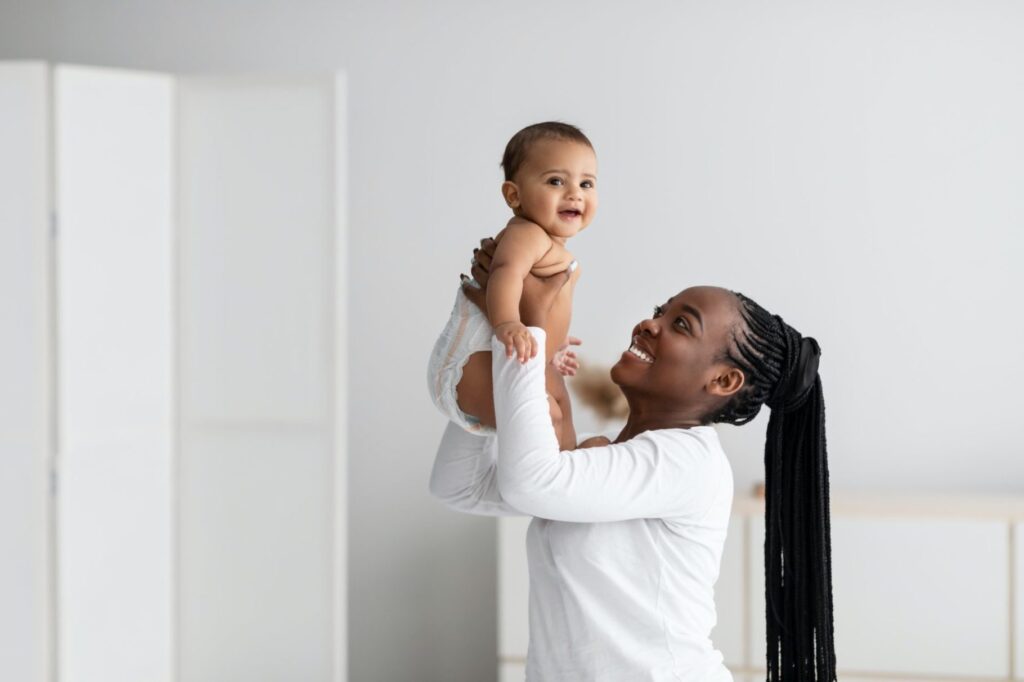 black woman playing with her cute little baby at home e1634117912841